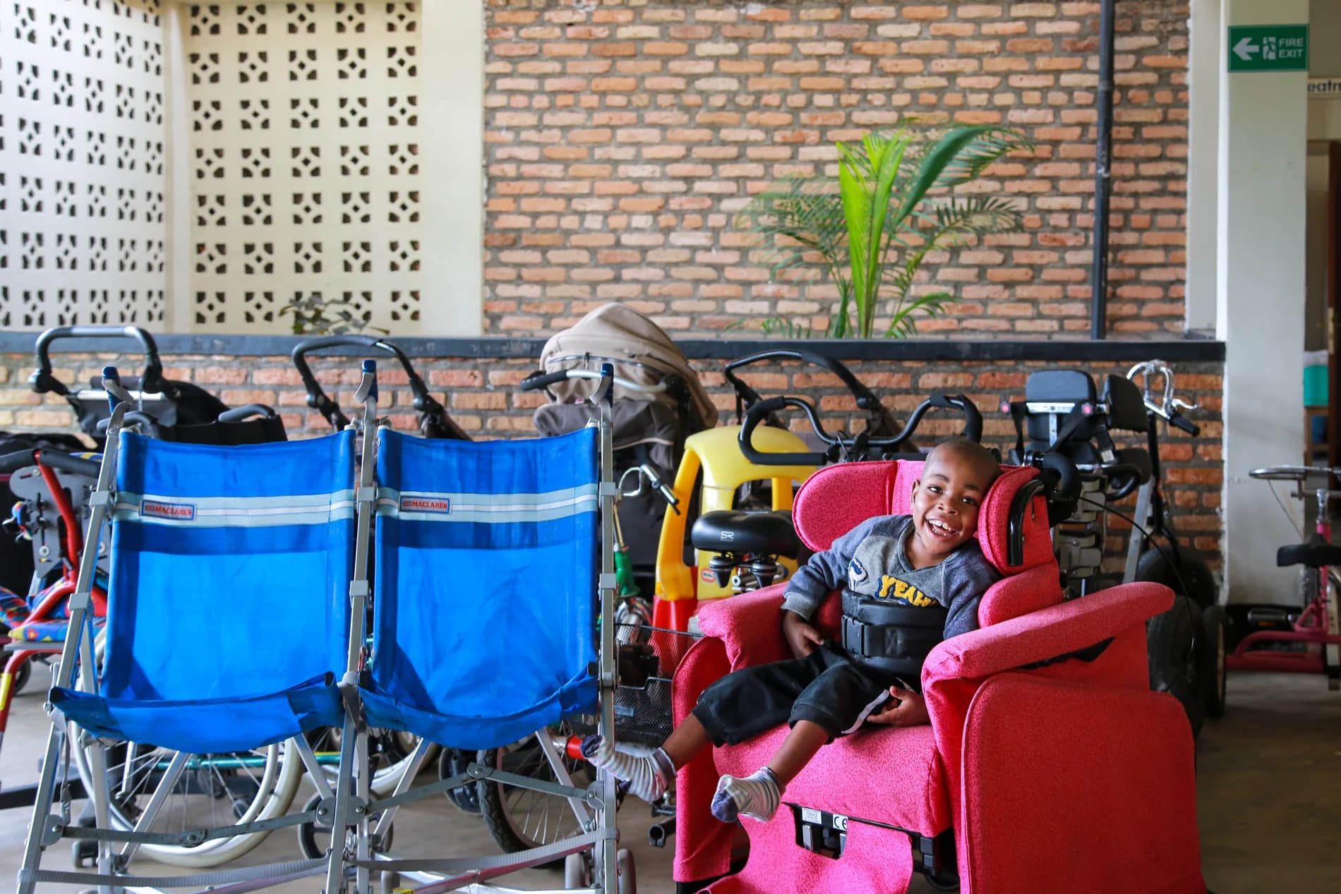 A smiling young patient seated in adaptive equipment beside mobility devices at the ASFA center