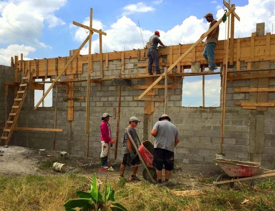 Local and volunteer builders assembling formwork and masonry walls at the M2535 Vocational Village construction site