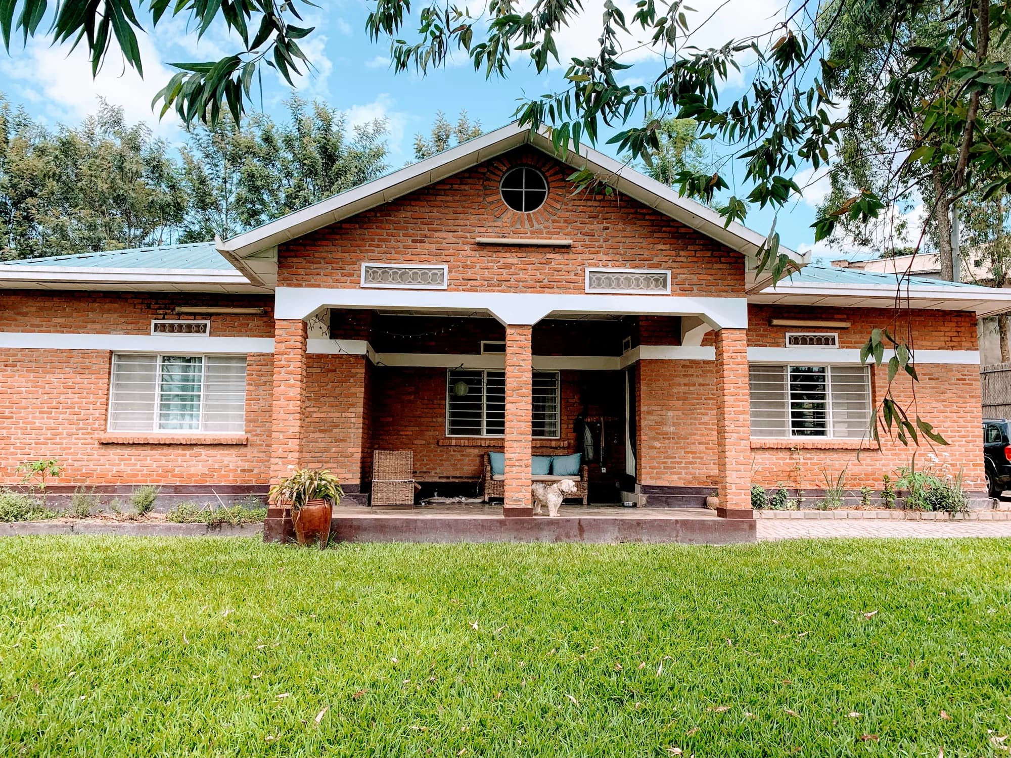 The completed NCM Guesthouse remodel, with its restored brick exterior, broad front veranda, and landscaped lawn in Kigali
