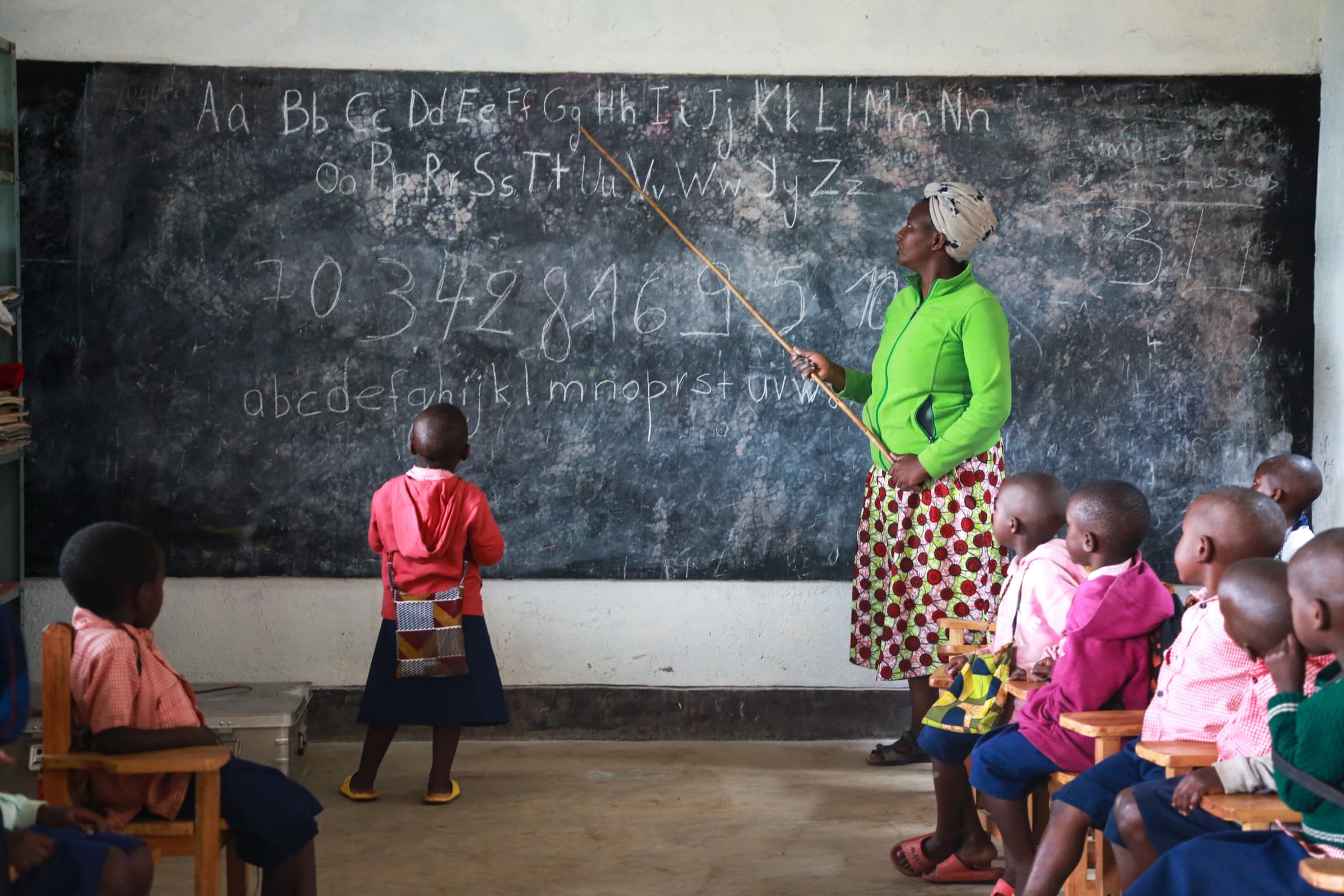 A teacher and student practicing the alphabet together at the Sunzu Village library blackboard