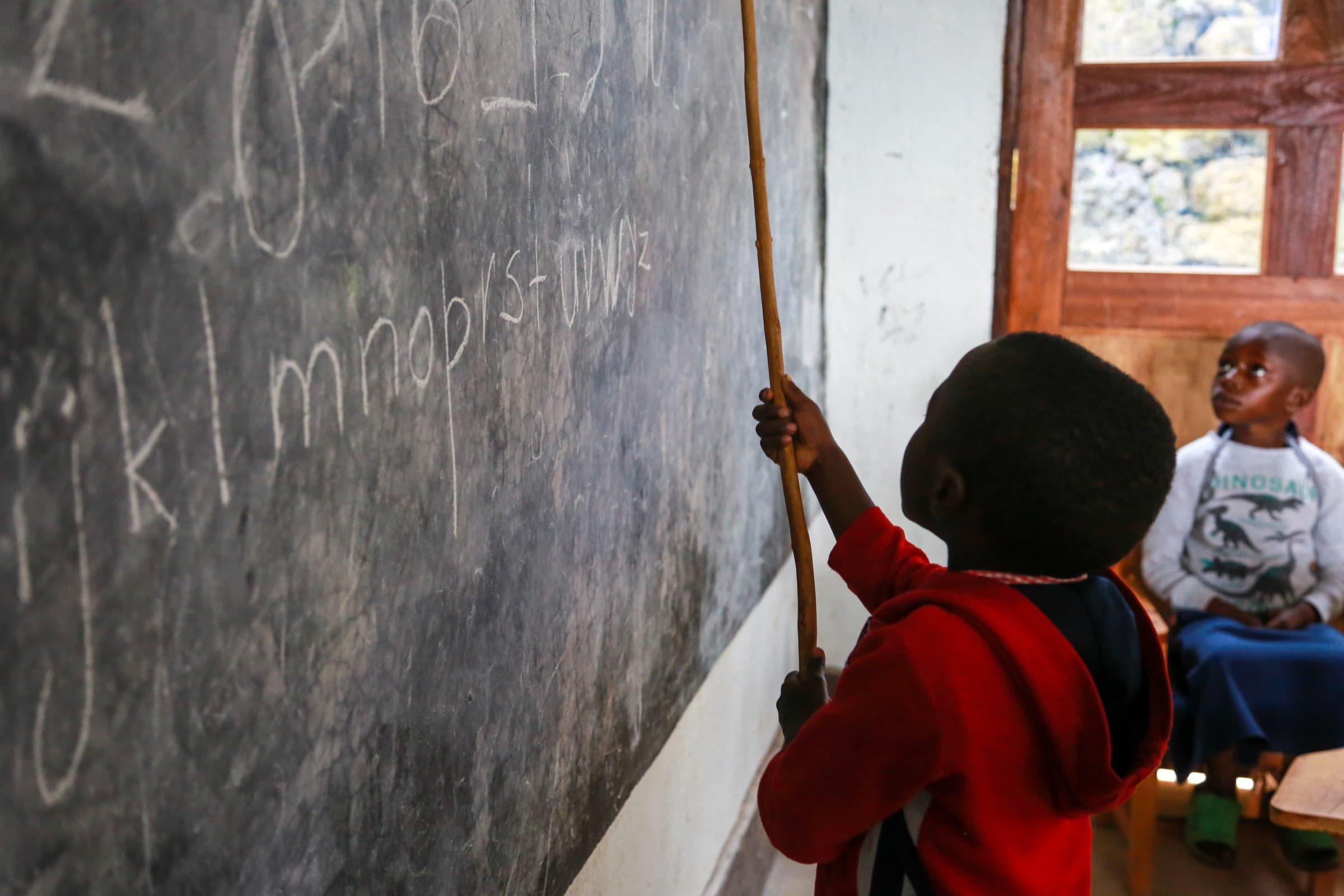 A child pointing to letters written on the Sunzu Village library blackboard